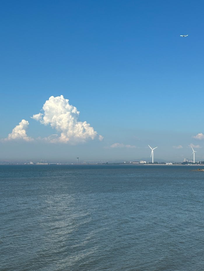 Tranquil coastal scene with wind turbines, airplane, and clear blue sky.